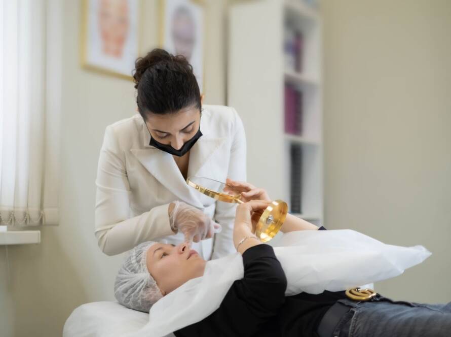A woman is laying down and looking into a mirror while specialist examens her face.