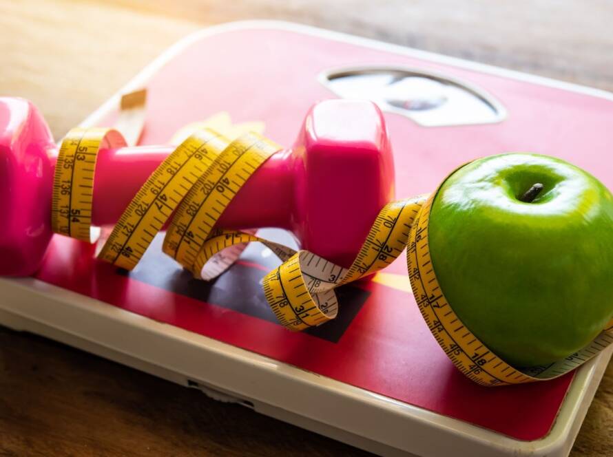 A weight and an apple sit on a scale wrapped in tailor’s measuring tape.