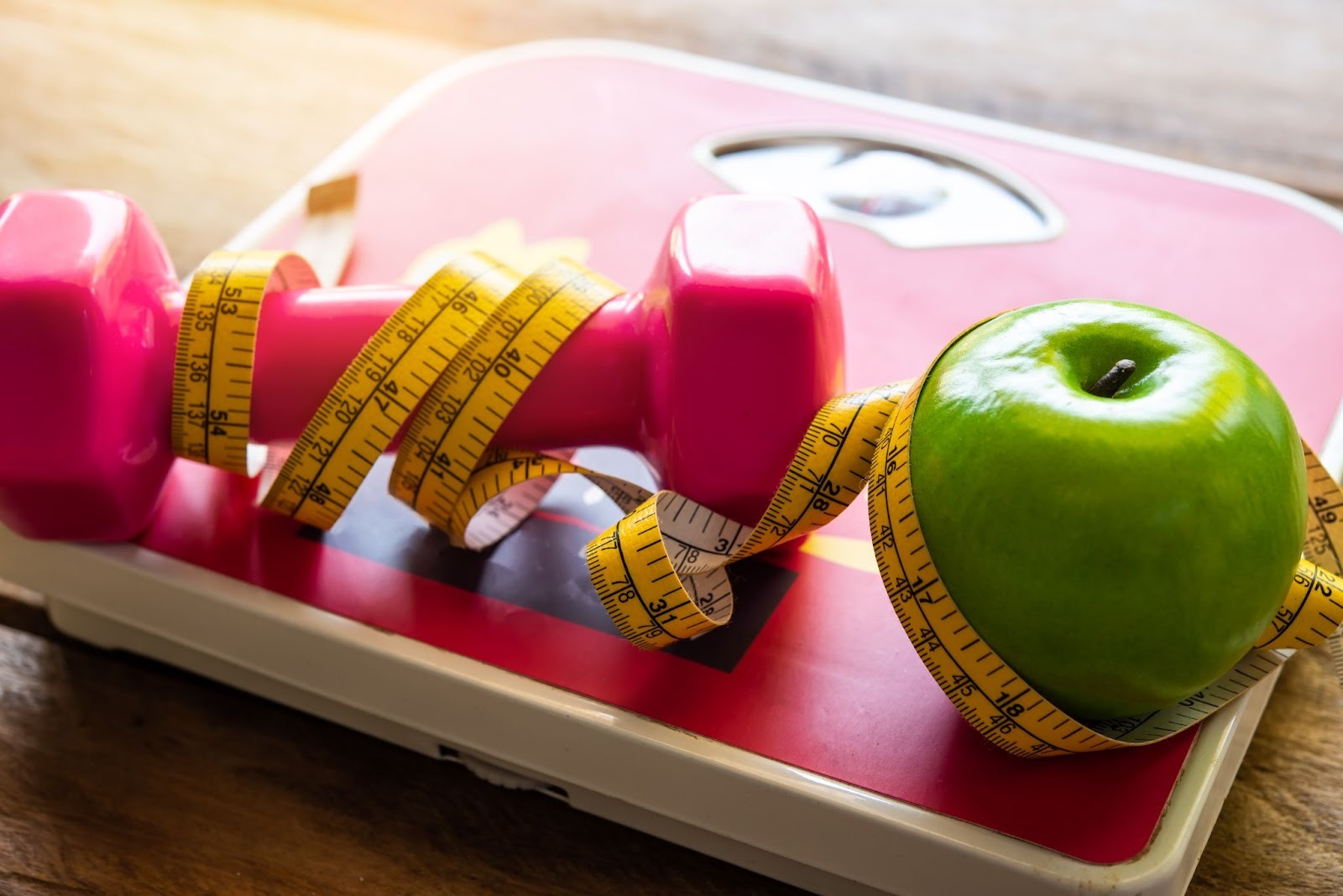 A weight and an apple sit on a scale wrapped in tailor’s measuring tape.