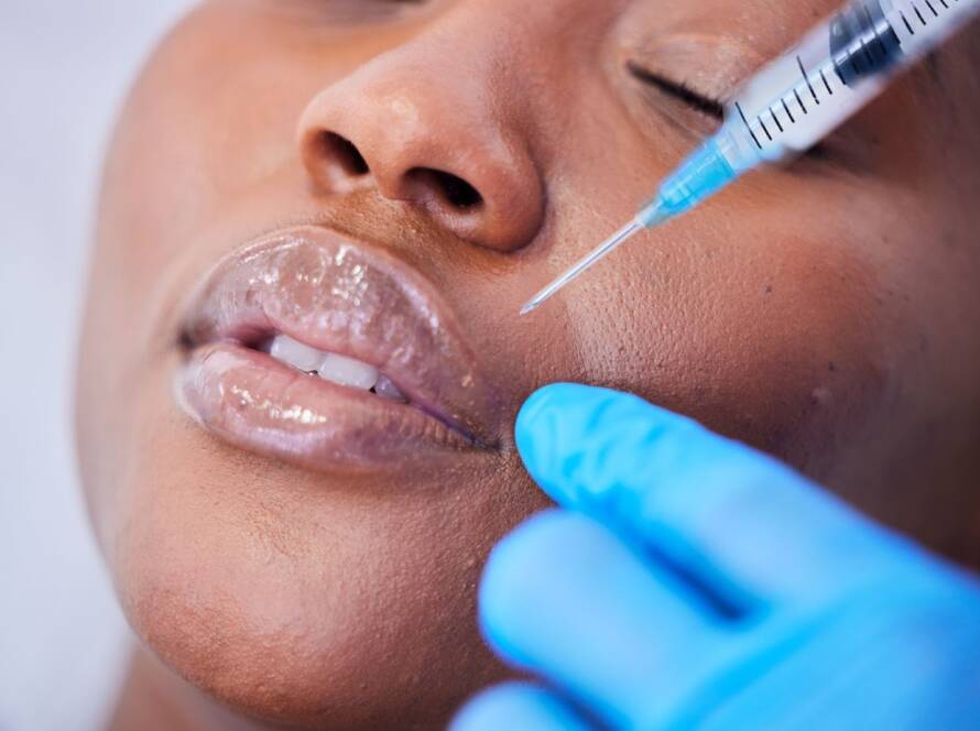 A doctor holds a syringe close to a woman’s face to administer a dermal filler.