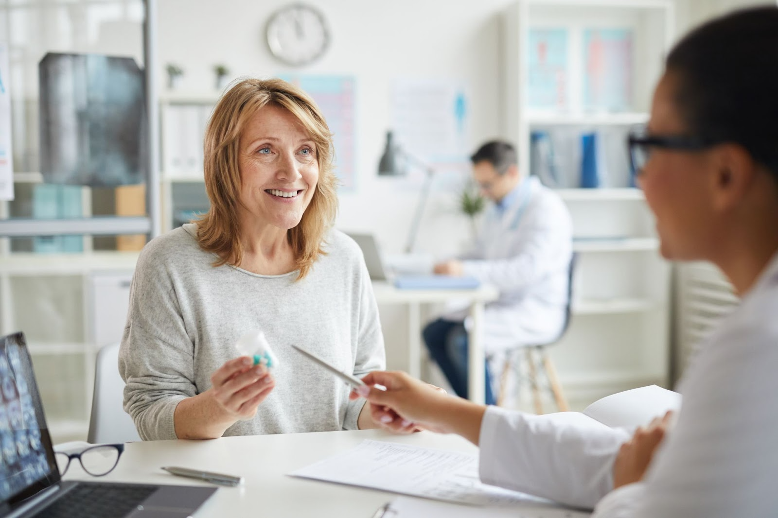 A female patient holds a medicine bottle while the doctor explains hormone replacement therapy.